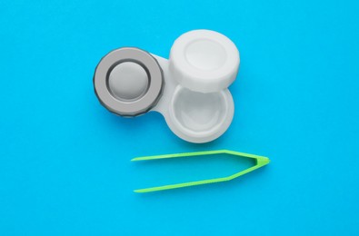 Photo of Case with contact lenses and tweezers on light blue background, flat lay