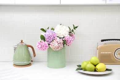 Beautiful hydrangea flowers, kettle and apples on light countertop