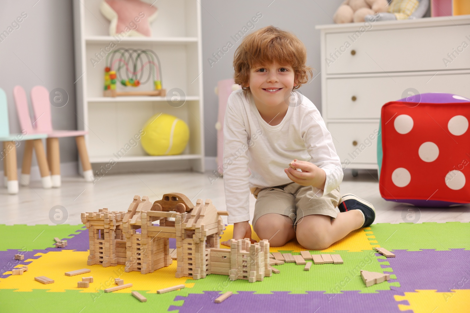 Photo of Little boy playing with wooden construction set on puzzle mat in room. Child's toy