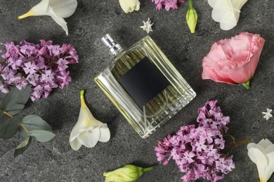 Bottle of luxury perfume and floral decor on dark grey table, flat lay