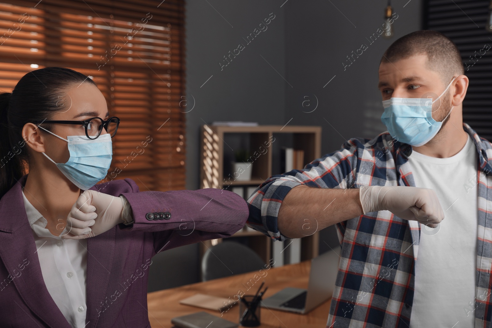 Photo of Office employees in masks greeting each other by bumping elbows at workplace