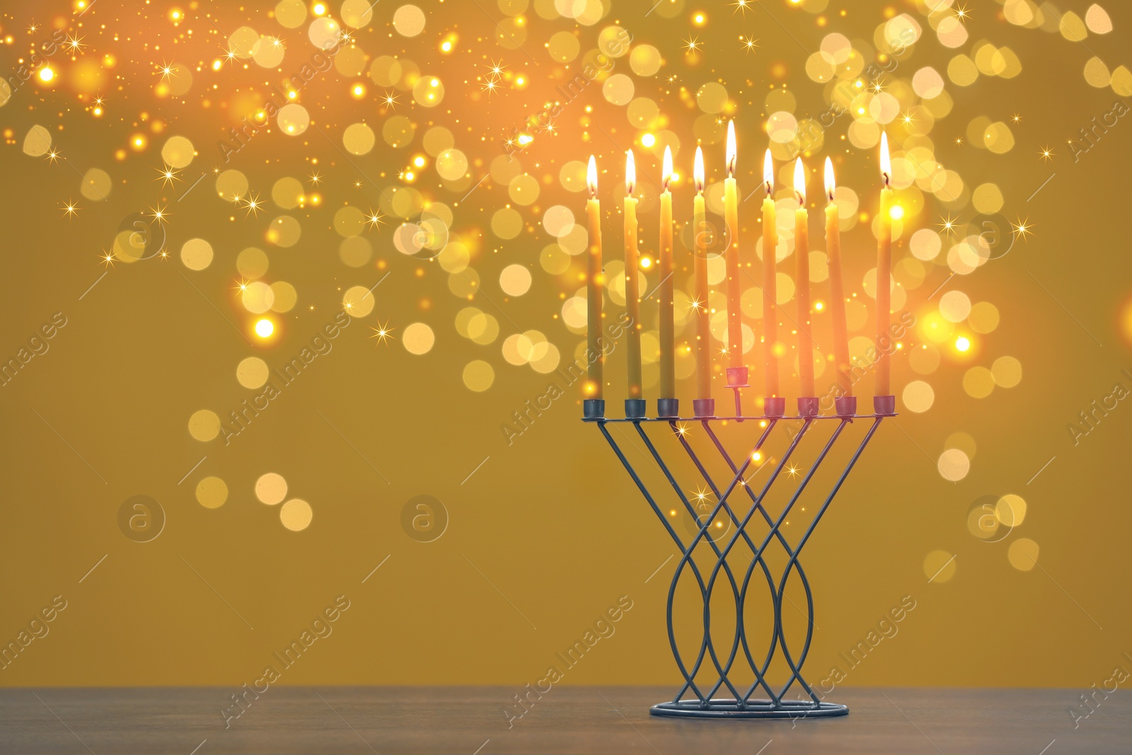 Image of Hanukkah celebration. Menorah with burning candles on table against goldenrod background with blurred lights, space for text