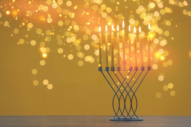 Hanukkah celebration. Menorah with burning candles on table against goldenrod background with blurred lights, space for text