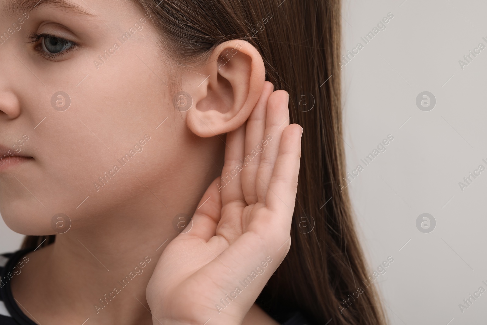 Photo of Little girl with hearing problem on grey background, closeup. Space for text