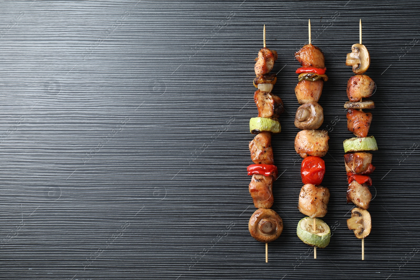 Photo of Delicious shish kebabs with vegetables on black table, top view. Space for text