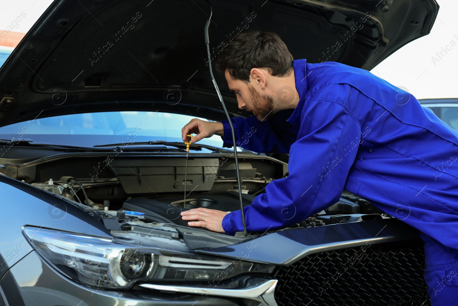 Photo of Worker checking motor oil level with dipstick outdoors