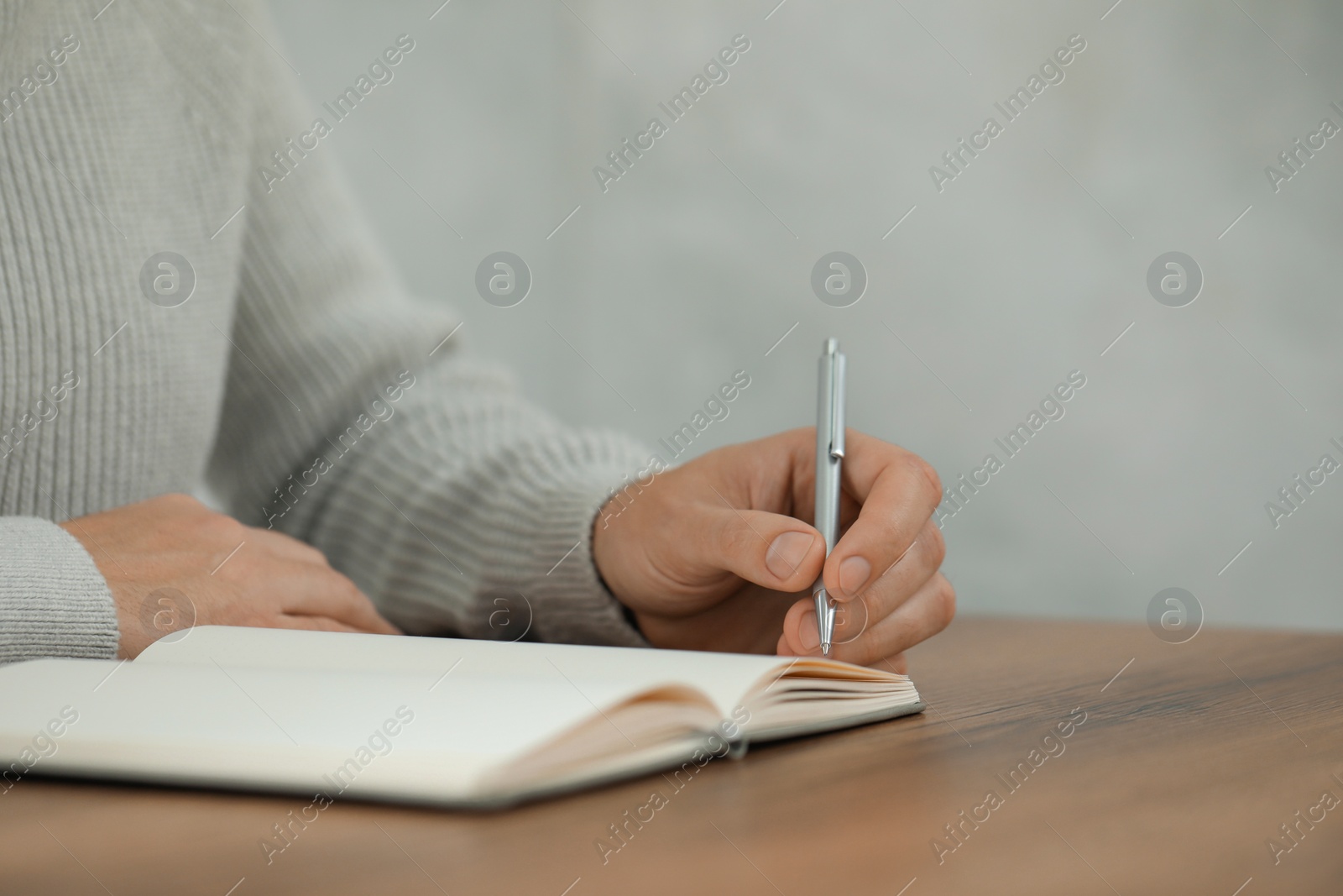 Photo of Man writing in notebook at wooden table, closeup