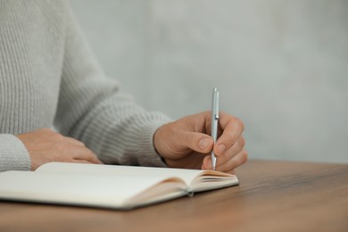 Photo of Man writing in notebook at wooden table, closeup