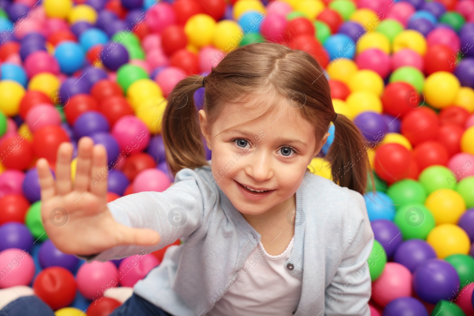 Photo of Happy little girl sitting on colorful balls in ball pit