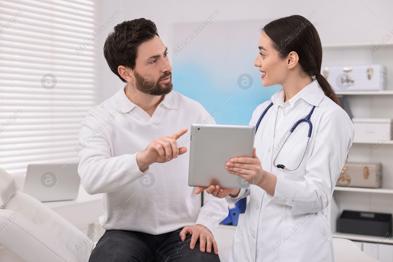 Photo of Doctor with tablet consulting patient during appointment in clinic