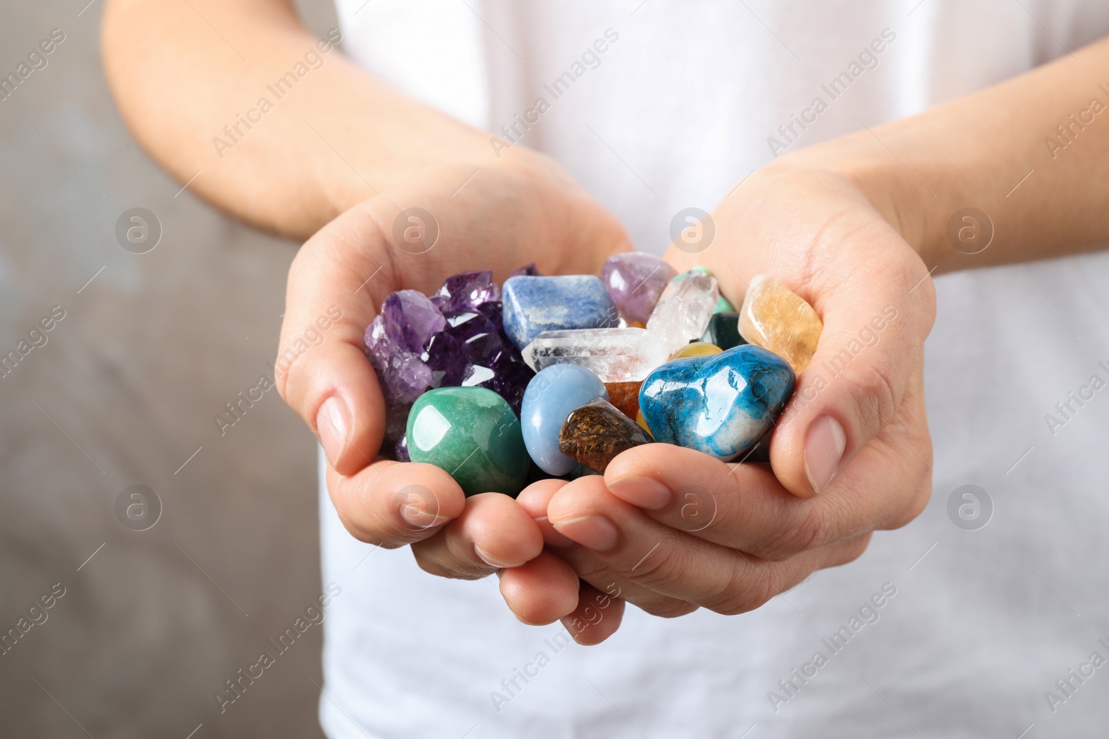 Photo of Young woman holding many beautiful gemstones on beige background, closeup