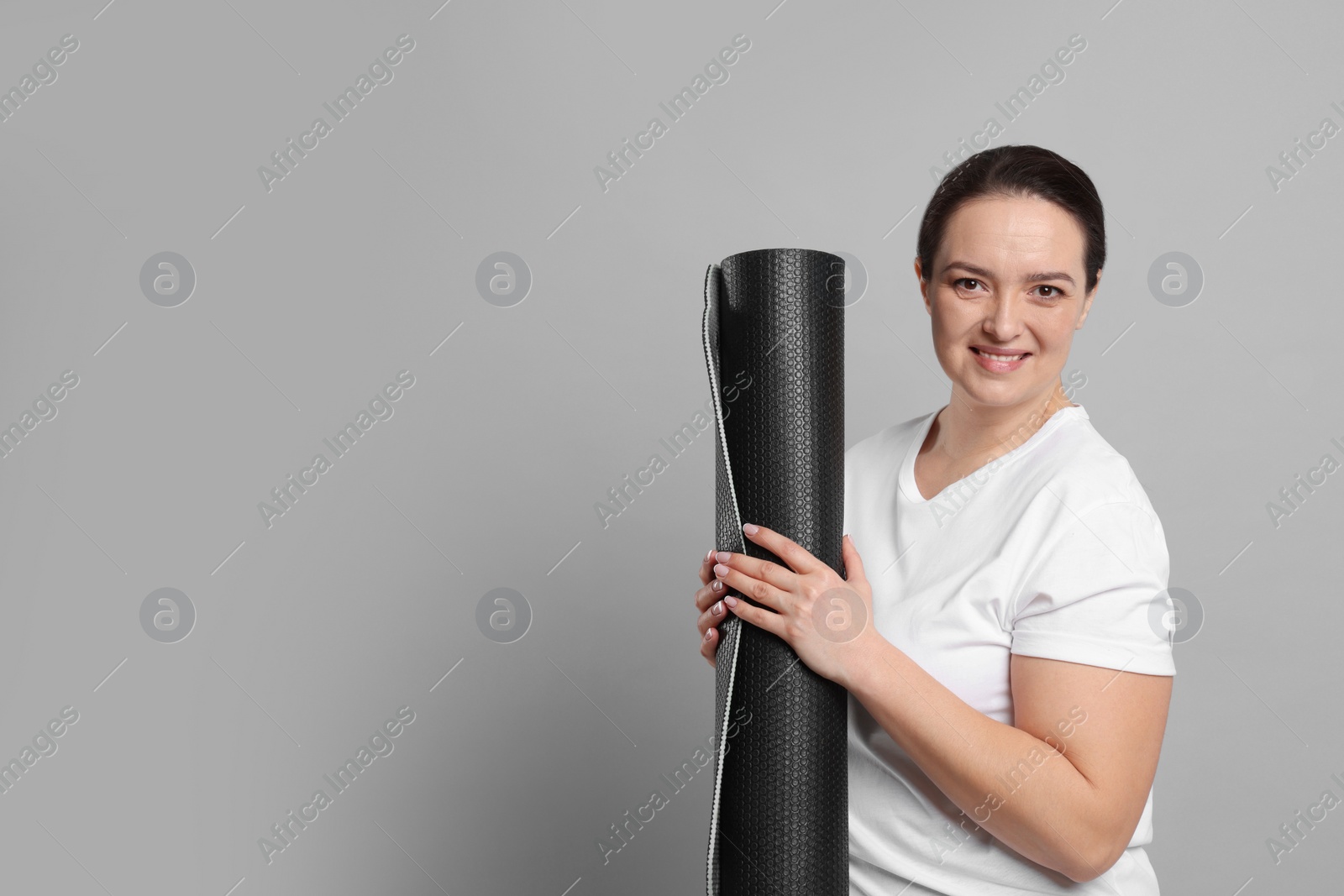 Photo of Happy overweight woman with yoga mat on grey background, space for text