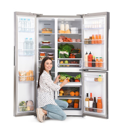 Young woman near open refrigerator on white background