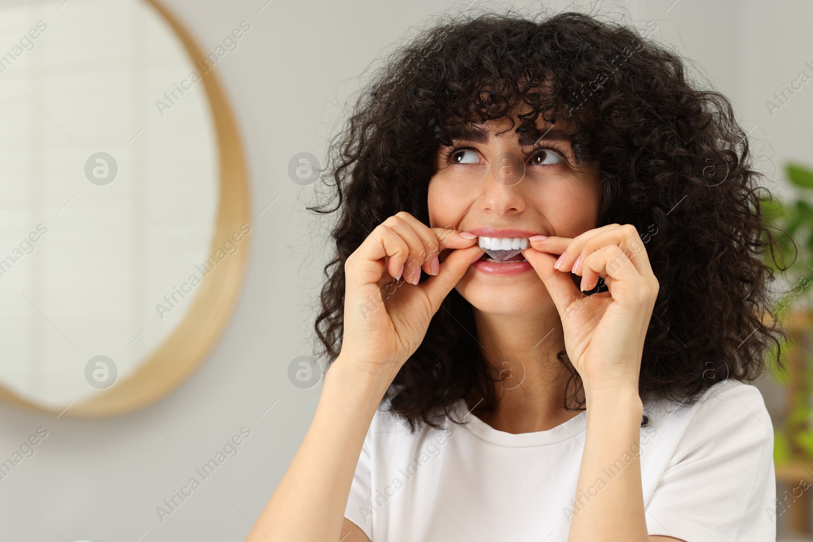 Photo of Young woman applying whitening strip on her teeth indoors, space for text