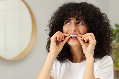 Young woman applying whitening strip on her teeth indoors, space for text