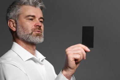 Handsome man holding blank business card on grey background