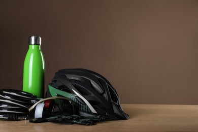 Photo of Different cycling accessories on wooden table against brown background, space for text