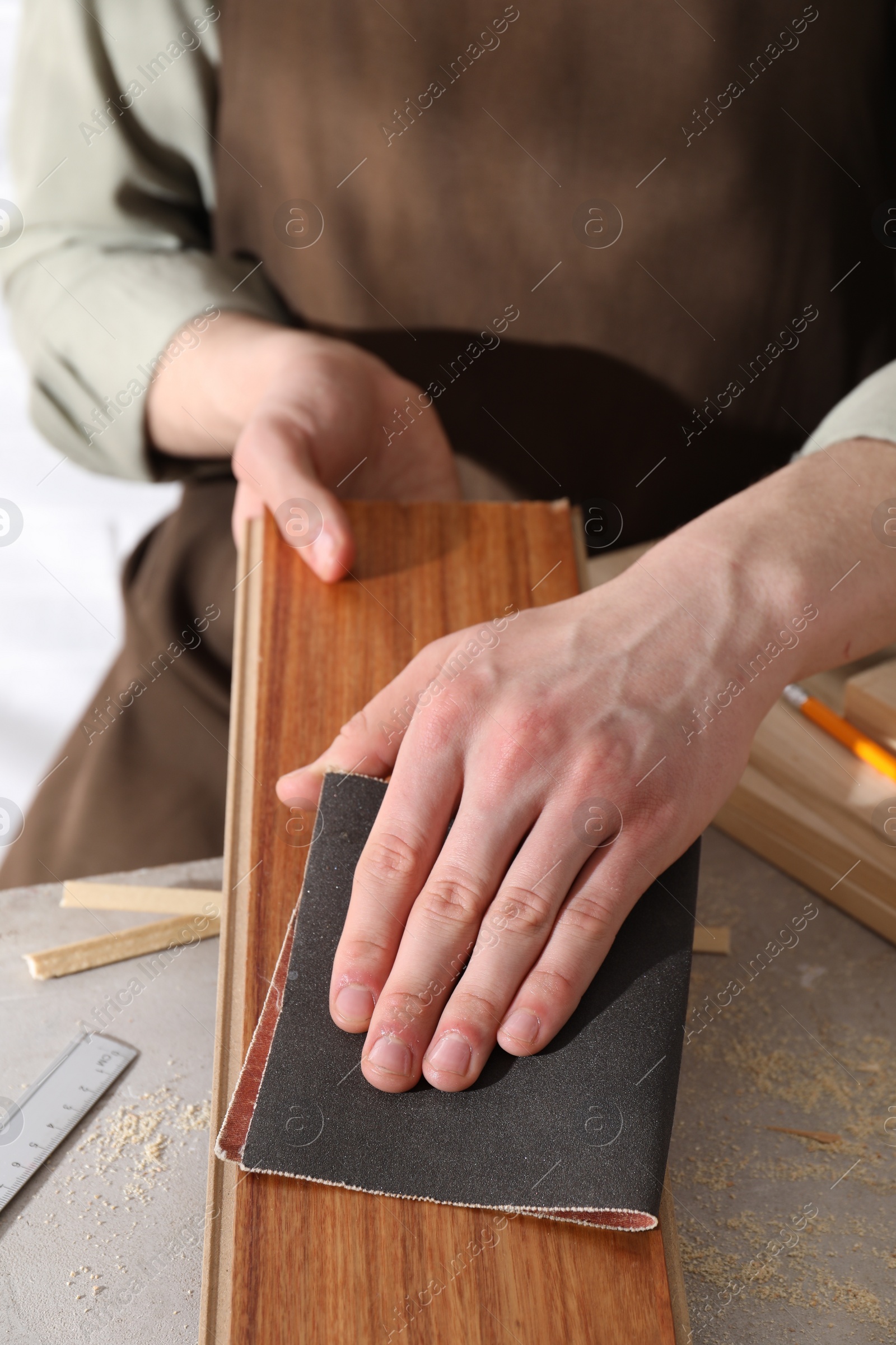 Photo of Man polishing wooden plank with sandpaper at grey table, closeup