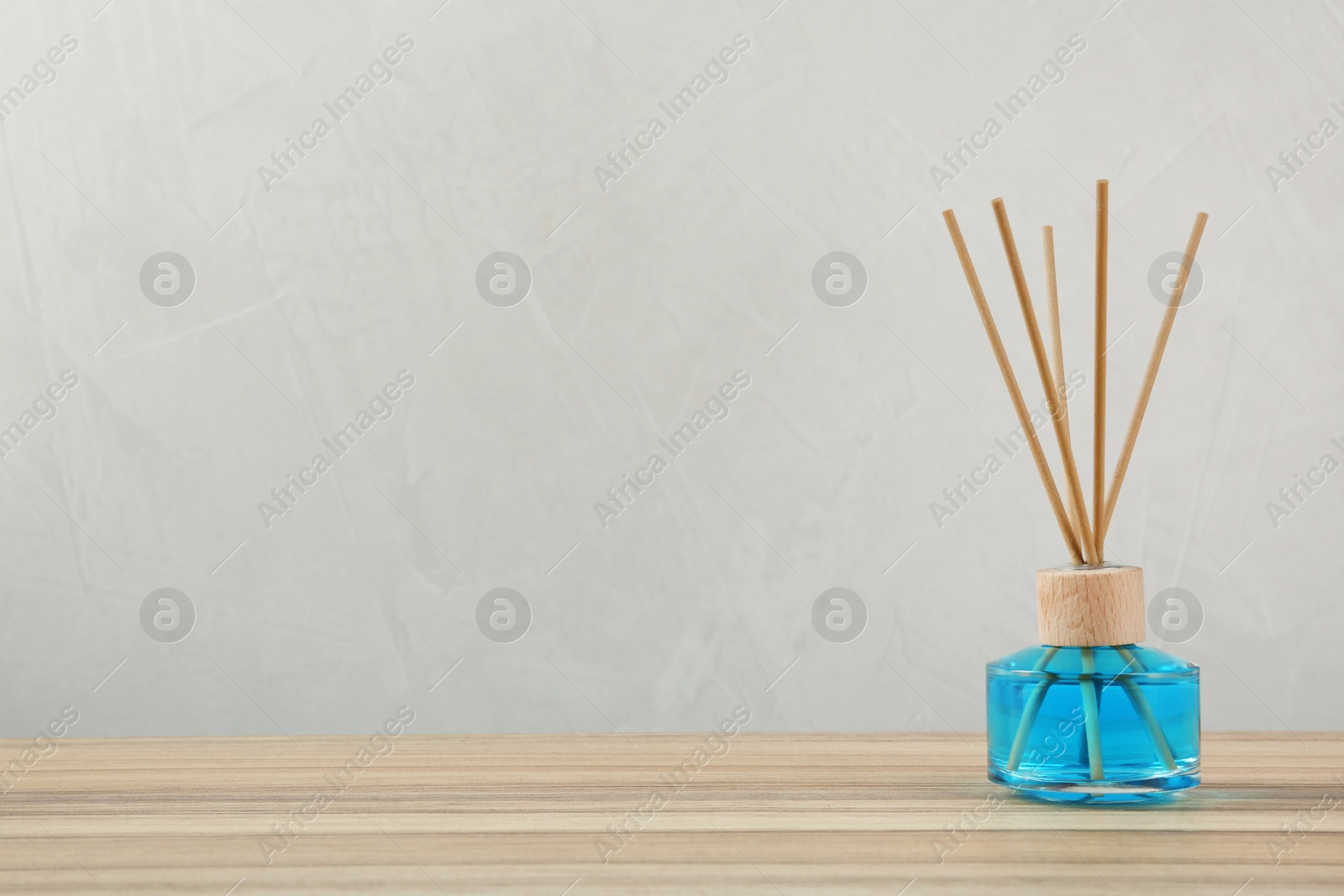 Photo of Reed air freshener on wooden table against grey background, space for text