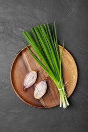 Photo of Bunch of fresh green onion and halved bulb on black table, top view