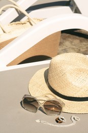Stylish hat, sunglasses and jewelry on grey sunbed outdoors, space for text