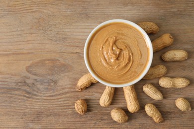 Photo of Delicious nut butter in bowl and peanuts on wooden table, top view. Space for text