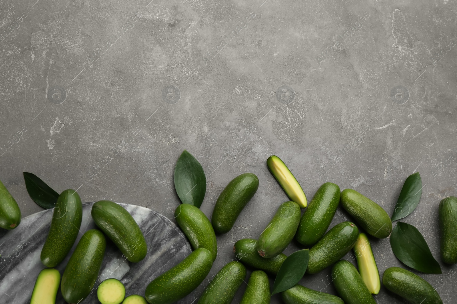 Photo of Whole and cut seedless avocados with green leaves on grey table, flat lay. Space for text