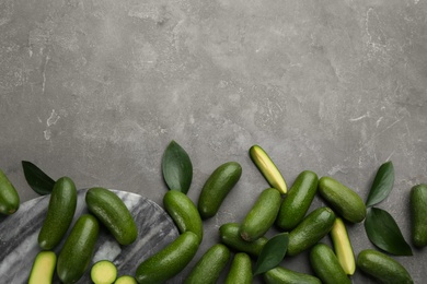 Photo of Whole and cut seedless avocados with green leaves on grey table, flat lay. Space for text