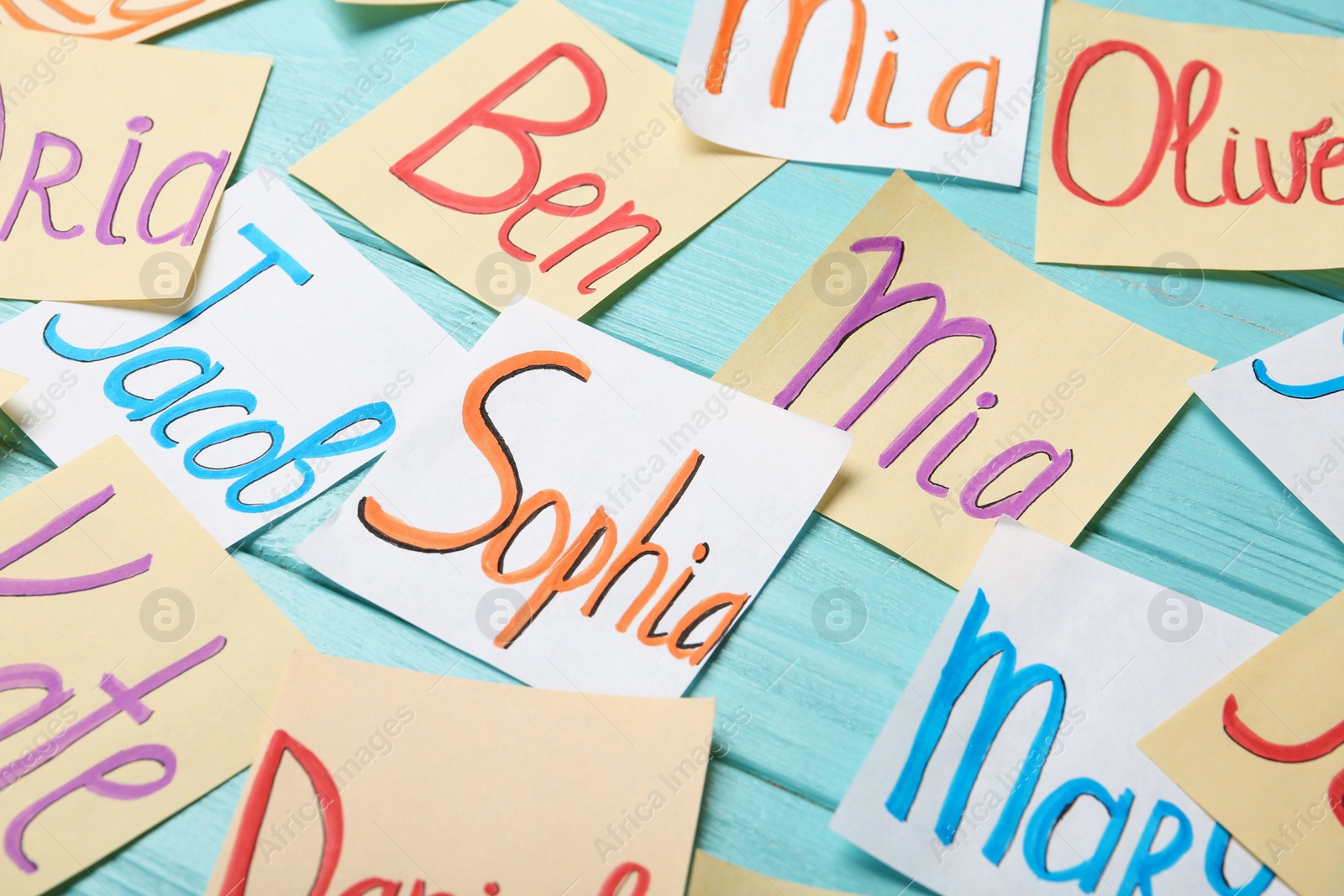 Photo of Paper notes with different baby names on light blue wooden table