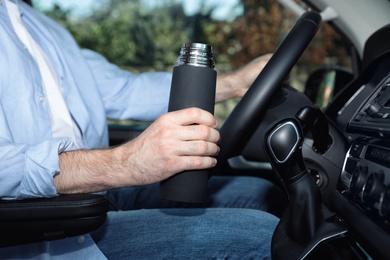 Man with thermos driving car, closeup view