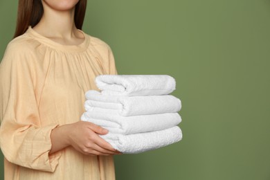 Photo of Woman holding folded soft terry towels on green background, closeup. Space for text