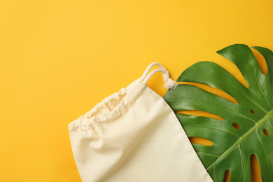 Photo of Cotton eco bag and leaf on yellow background, flat lay. Space for text