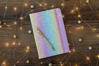 Photo of Stylish planner, pen and Christmas lights on wooden background, flat lay. New Year aims
