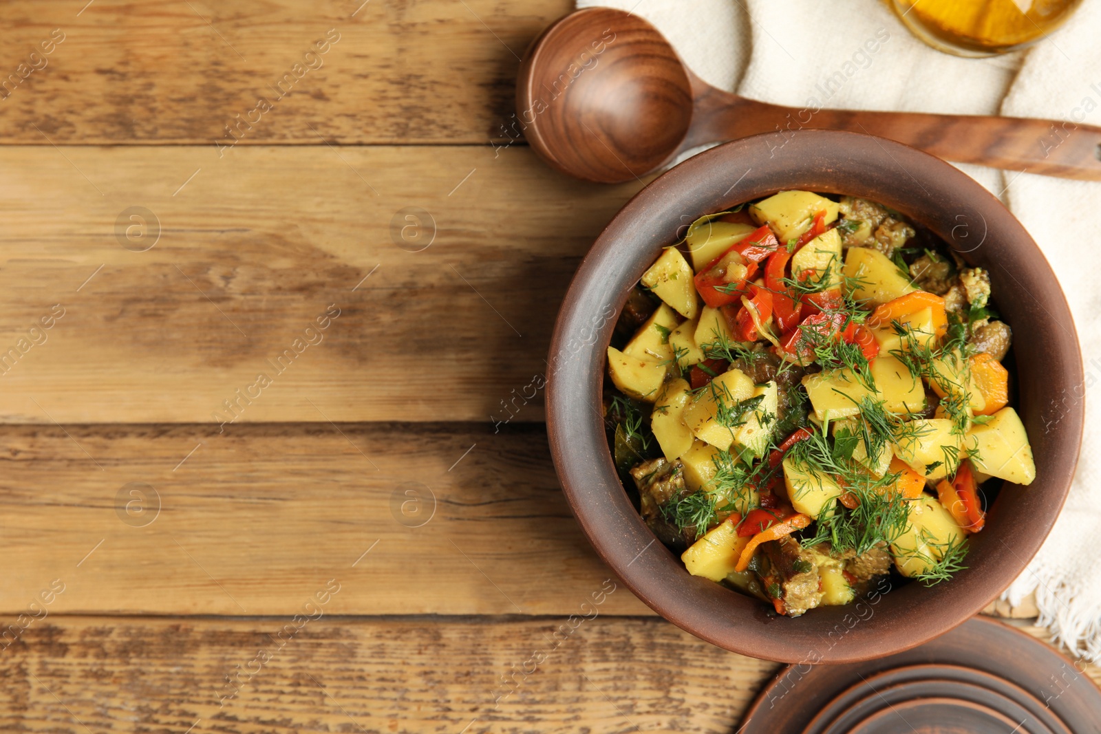 Photo of Tasty cooked dish with potatoes in earthenware served on wooden table, flat lay. Space for text