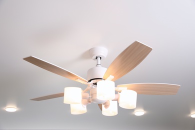Photo of Modern ceiling fan with lamps and wooden blades indoors
