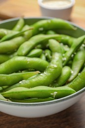 Photo of Bowl with green edamame beans in pods on wooden table, closeup