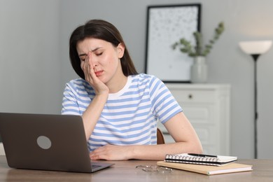 Overwhelmed woman sitting with laptop at table indoors