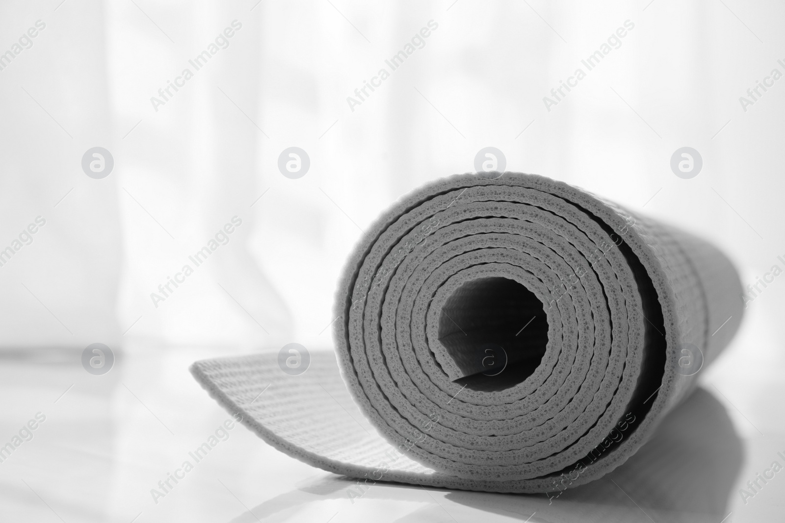 Photo of Rolled karemat or fitness mat on floor indoors, closeup. Space for text