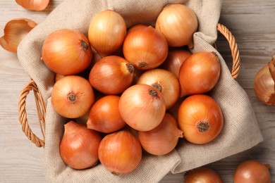 Wicker basket with many ripe onions on wooden table, top view