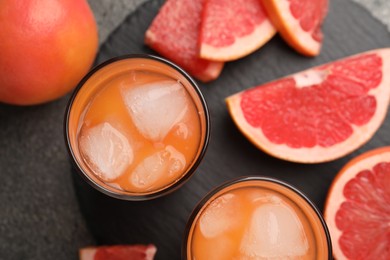 Photo of Tasty grapefruit drink with ice in glasses and fresh fruits on dark table, flat lay