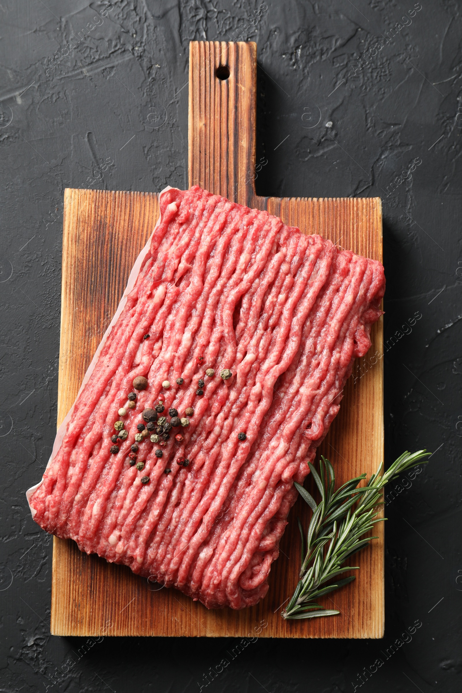 Photo of Raw ground meat, rosemary and peppercorns on black table, top view