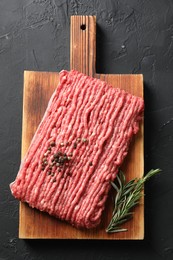 Raw ground meat, rosemary and peppercorns on black table, top view