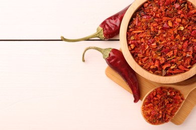 Photo of Chili pepper flakes and pods on white wooden table, flat lay. Space for text