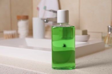 Photo of Fresh mouthwash in bottle on countertop near sink in bathroom, closeup