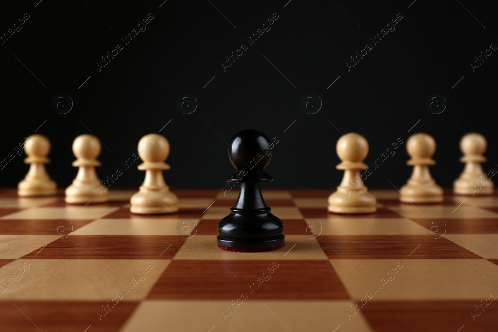 Photo of Black pawn in front of white ones on wooden chess board against dark background