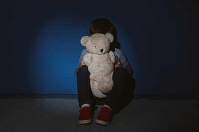 Photo of Little boy with teddy bear near blue wall. Domestic violence concept