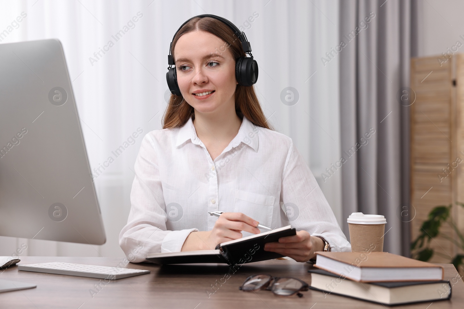 Photo of E-learning. Young woman taking notes during online lesson at wooden table indoors