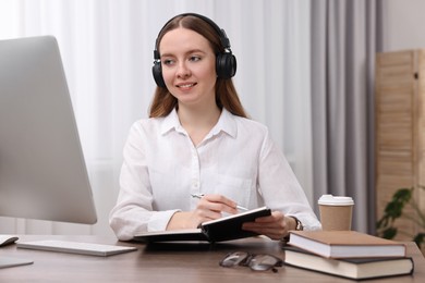 E-learning. Young woman taking notes during online lesson at wooden table indoors