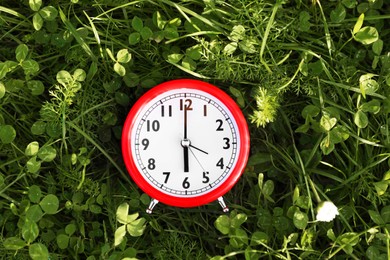 Photo of Red alarm clock on green grass outdoors, top view