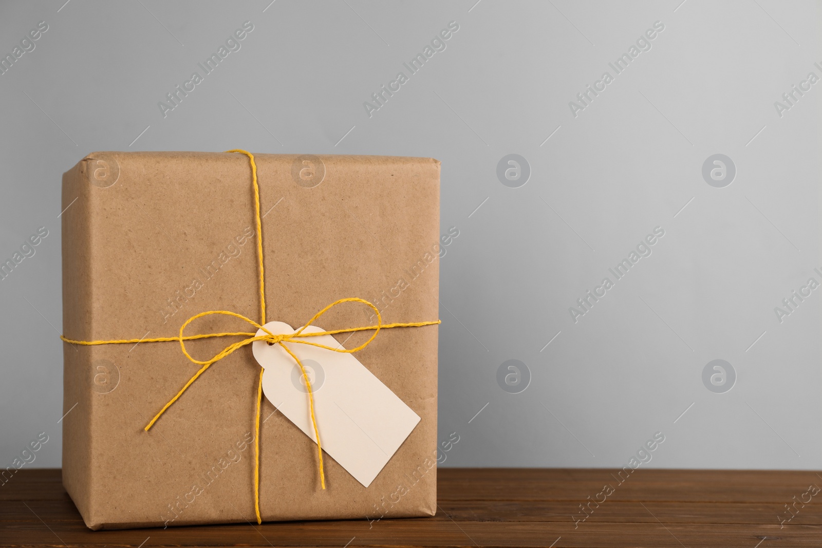 Photo of Parcel wrapped in kraft paper with tag on wooden table against light grey background, space for text